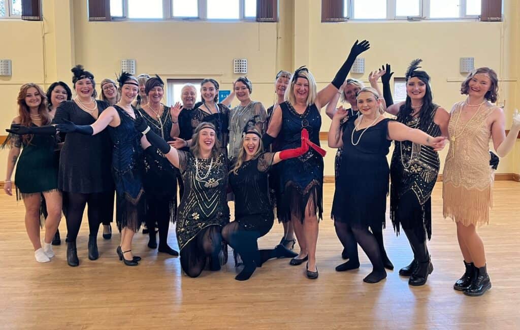 Friends laughing and dancing during a 1920s themed hen do, dressed in flapper outfits at a fun Charleston dance party – a perfect Great Gatsby hen party activity.